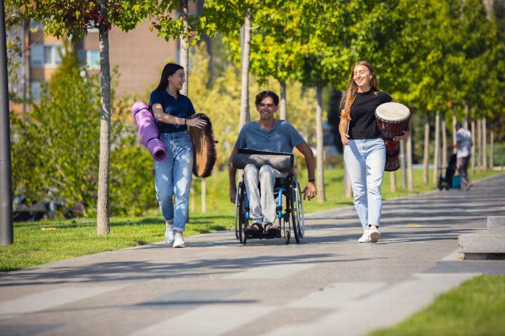 Tres personas paseando al aire libre, una de ellas con discapacidad motriz